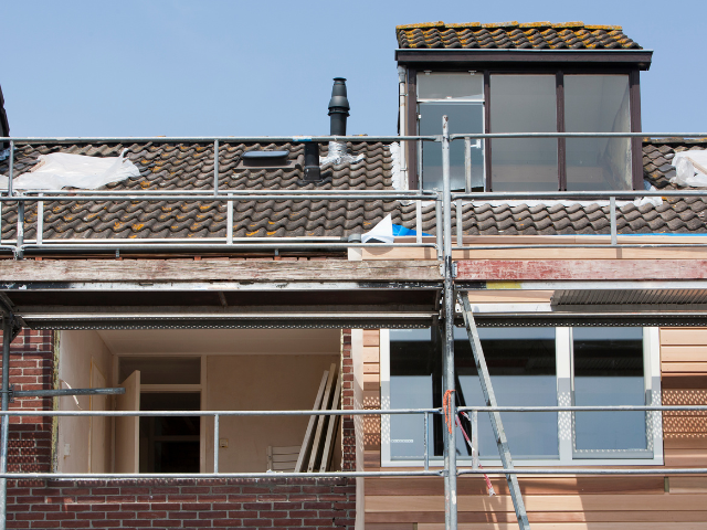 Chantier de construction avec échafaudage autour d'un bâtiment en briques, fenêtres et lucarne sur le toit.