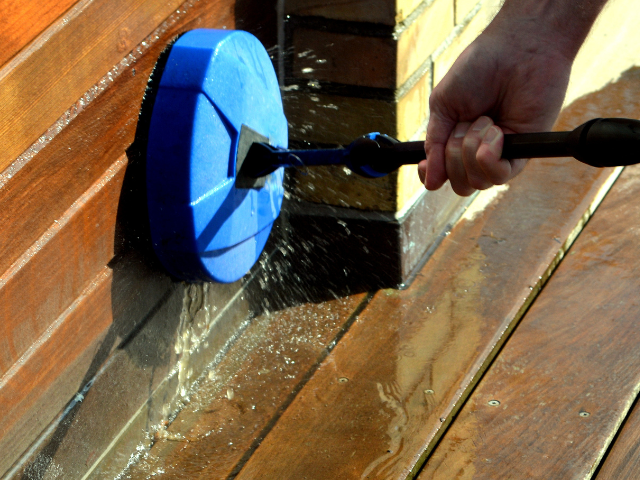 Une personne utilisant un nettoyeur de terrasse rotatif bleu, lavant une terrasse en bois.