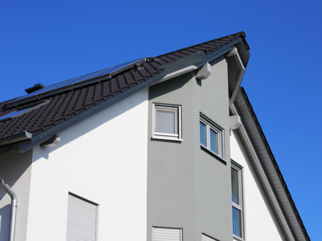 Maison moderne à deux étages avec un extérieur gris et blanc contre un ciel bleu clair.
