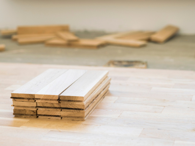Pile de planches de parquet sur un plancher en bois clair, avec des planches éparpillées en arrière-plan.
