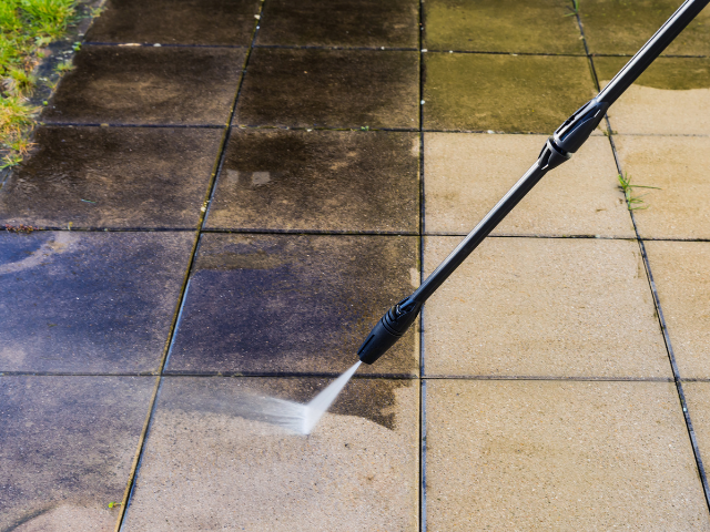 Nettoyeur haute pression nettoyant un patio sale et sombre, révélant un béton propre et de couleur claire.
