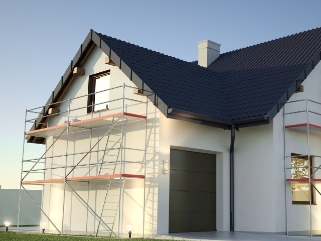 Extérieur de maison avec échafaudage à rénover; stuc blanc, toiture noire et porte de garage.