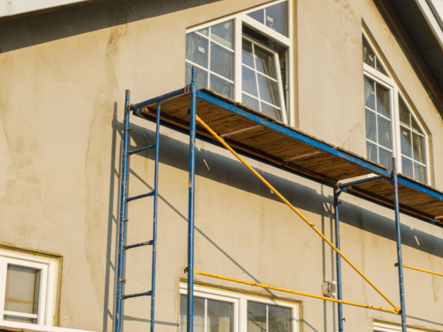 Échafaudage à côté d'un bâtiment avec fenêtres. Le bâtiment est revêtu d'un revêtement en stuc clair.