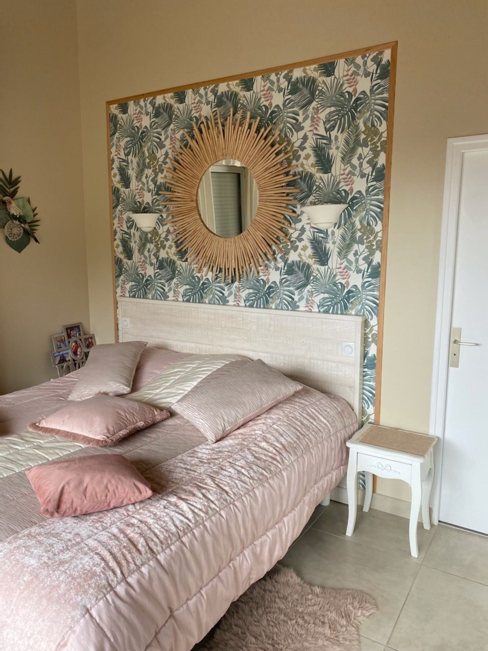 Chambre avec lit, papier peint floral, miroir soleil et table de chevet. Couleurs rose et crème.