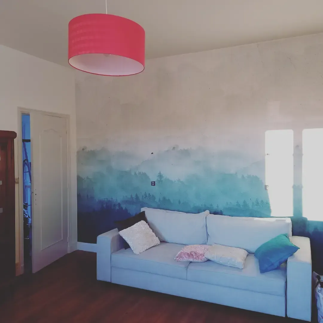 Chambre avec un canapé bleu clair, une fresque murale bleue et blanche et un abat-jour rose.