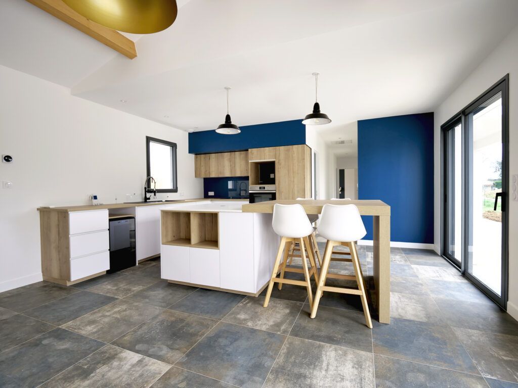 Cuisine moderne avec mur d'accent bleu, îlot avec tabourets, armoires en bois clair et portes coulissantes en verre.