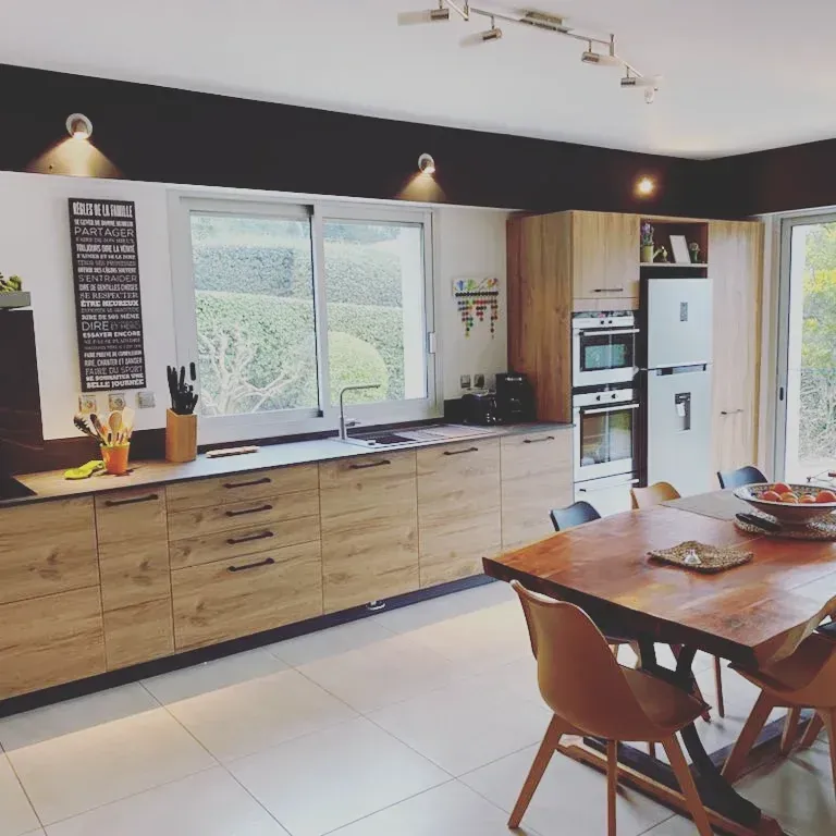 Cuisine moderne avec armoires en bois, comptoirs noirs et une grande table à manger en bois.