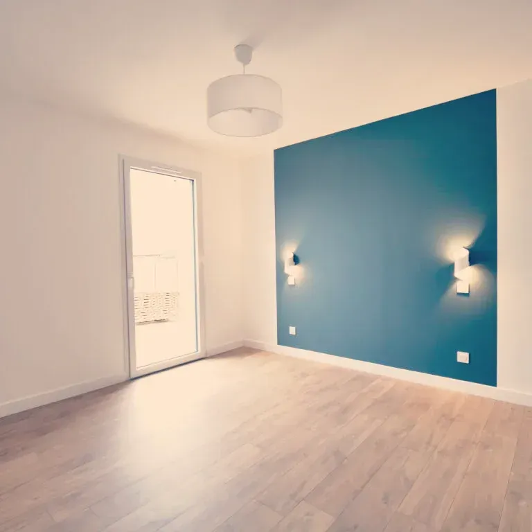 Pièce vide avec parquet, mur d'accent turquoise et porte blanche. Deux appliques encadrent le mur d'accent.
