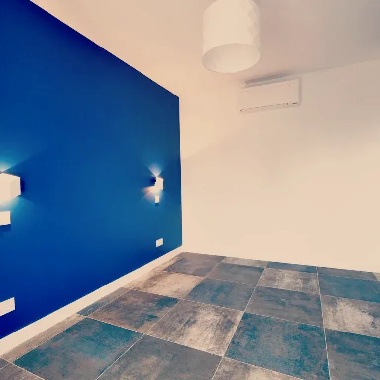 Mur d'accent bleu avec des lumières cubiques dans une pièce vide, murs blancs, sol en carrelage bleu et gris.