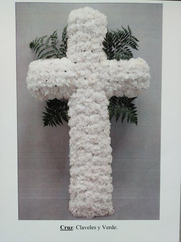 Cruz floral blanca con hojas verdes en una sencilla composición para interiores.