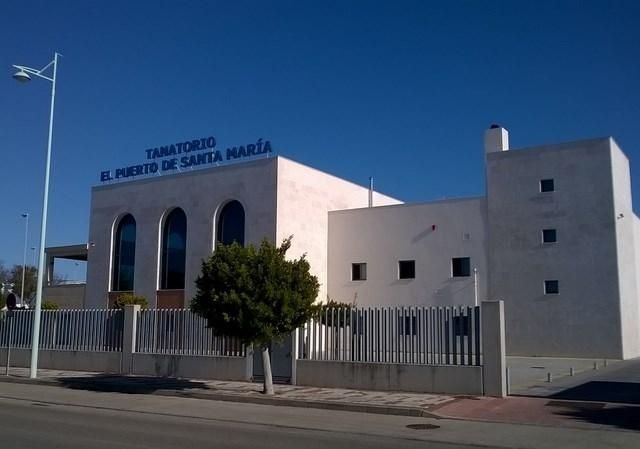 Exterior de un moderno edificio blanco con letrero en español y una entrada vallada bajo un cielo azul despejado.