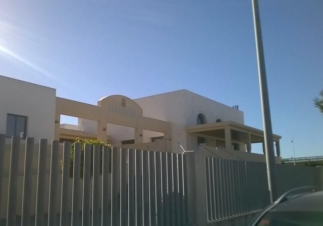Casa moderna detrás de una valla metálica bajo un cielo azul brillante.