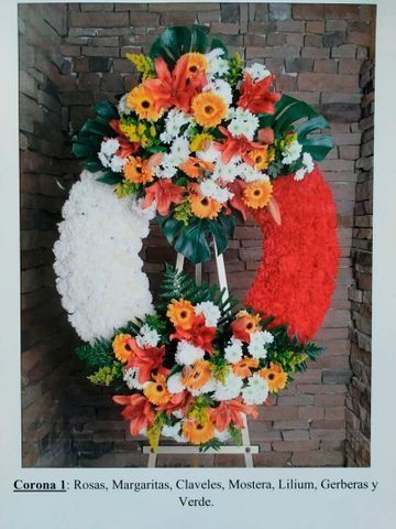 Corona floral con los colores de la bandera mexicana y una cinta conmemorativa en una pared de ladrillos.