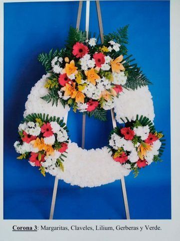 Corona floral blanca con flores de colores sobre fondo azul, colgando de cuerdas.