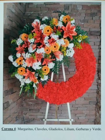 Corona floral con flores naranjas, blancas y amarillas sobre una pared de ladrillos, con forma de media luna roja.