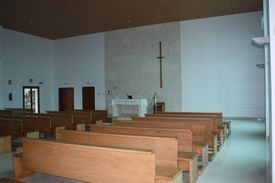 Interior de la iglesia con bancos de madera, altar y cruz en la pared frontal.