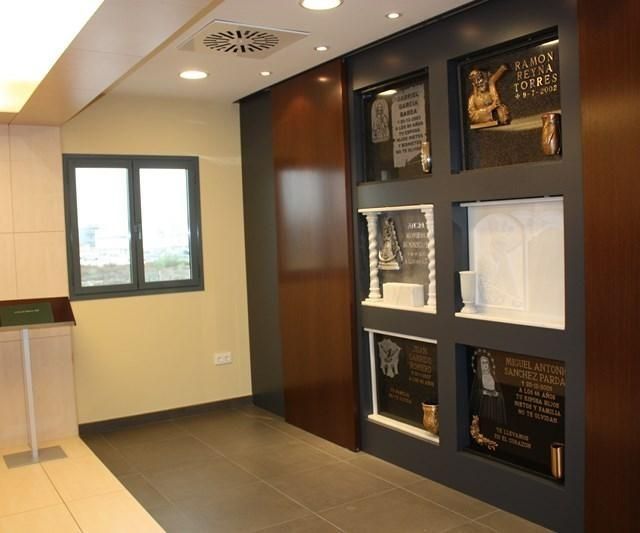 Pasillo interior moderno con nichos de exposición, placas enmarcadas y una ventana a la izquierda.