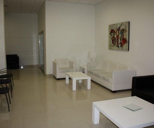 Moderna sala de estar blanca con sofás, mesas de centro, cuadros y una hilera de sillas negras a lo largo de la pared izquierda.