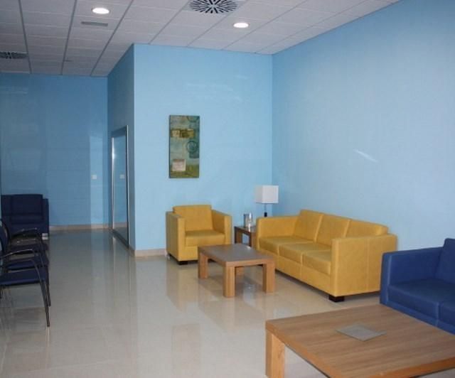 Sala de espera vacía con paredes azules, sillas amarillas y azules y pequeñas mesas de madera.