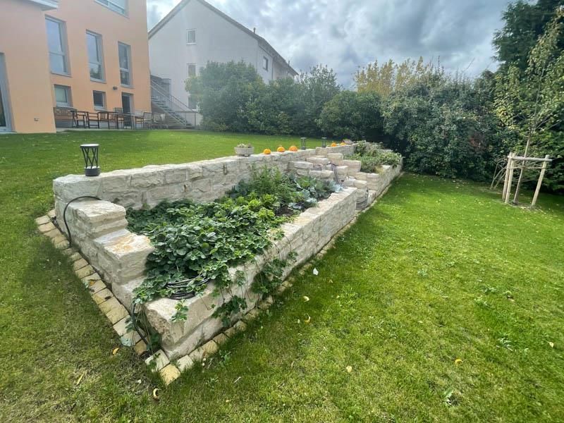 Ein Garten mit einer Backsteinmauer und Pflanzen darin vor einem Haus.