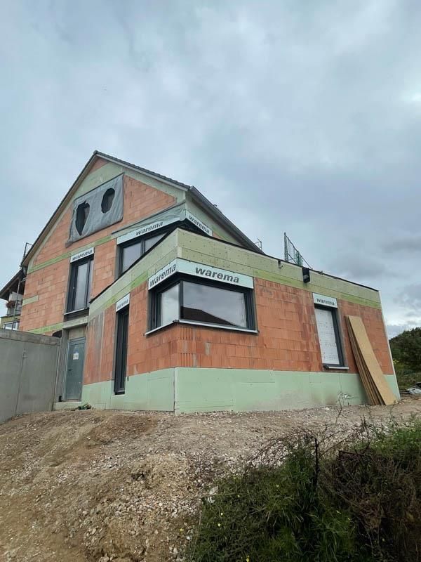 Auf einem Erdhügel wird ein Backsteinhaus gebaut.