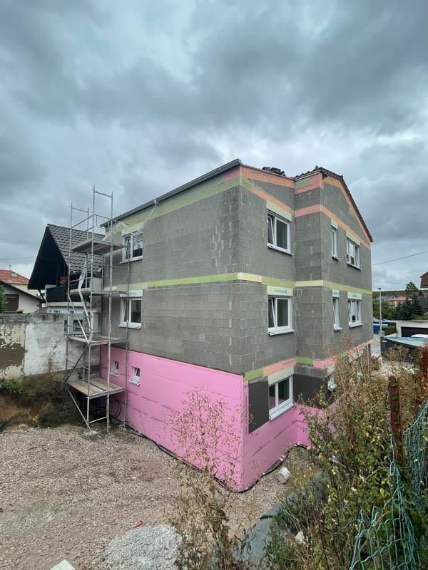 Es wird ein Gebäude mit rosa Isolierung und Gerüst gebaut.