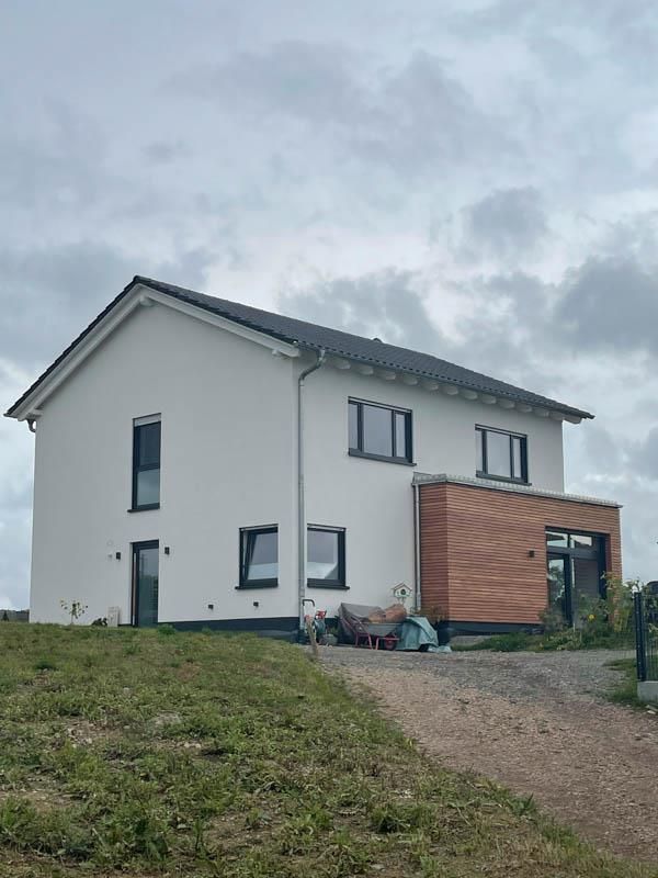 Auf einem grasbewachsenen Hügel steht ein weißes Haus mit schwarzem Dach.