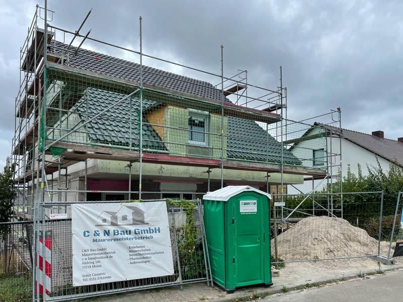Ein im Bau befindliches Haus mit Gerüst und einer grünen Mobiltoilette
