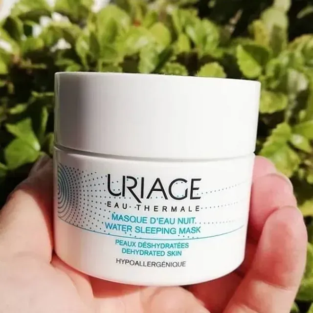 Una persona sostiene un frasco de mascarilla para dormir de agua Uriage.