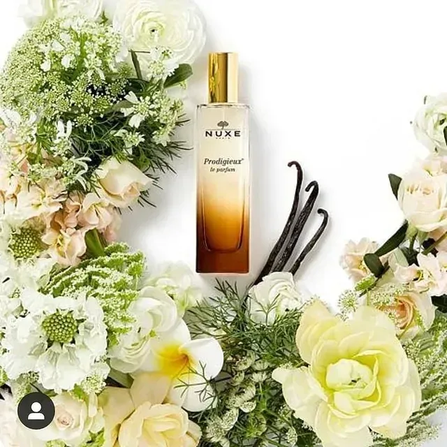 Un frasco de perfume Nuxe está rodeado de flores.