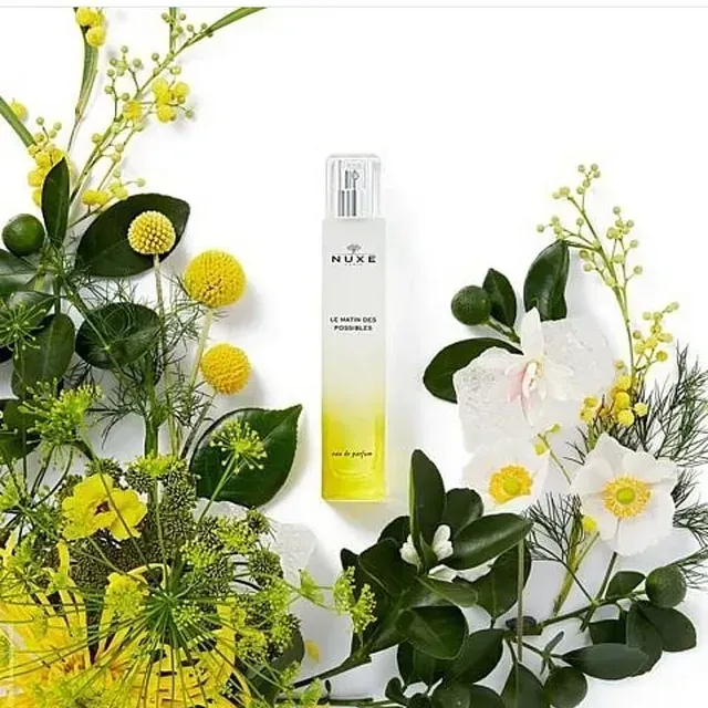 Una botella de Nuxe rodeada de flores y hojas.