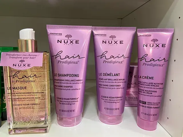 Hay cuatro botellas de productos capilares Nuxe en un estante.