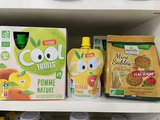 Un estante con una caja de frutas frescas y una bolsa de mini sables.
