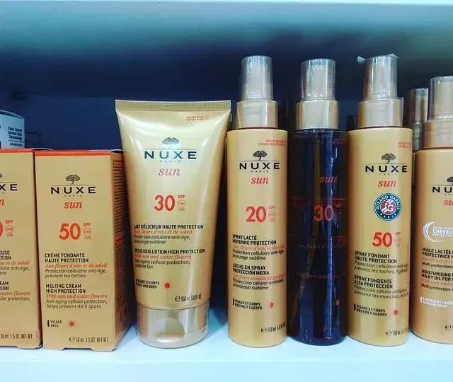 Varias botellas de productos Nuxe Sun están alineadas en un estante.