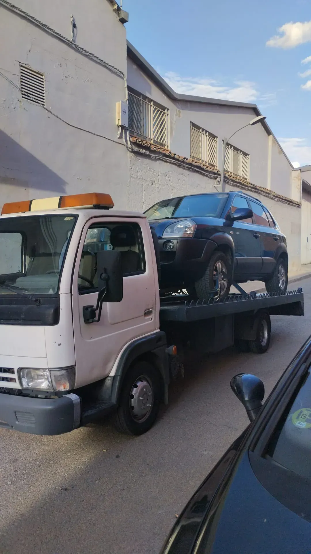 Grúa transportando una camioneta SUV negra en una calle estrecha frente a un edificio.
