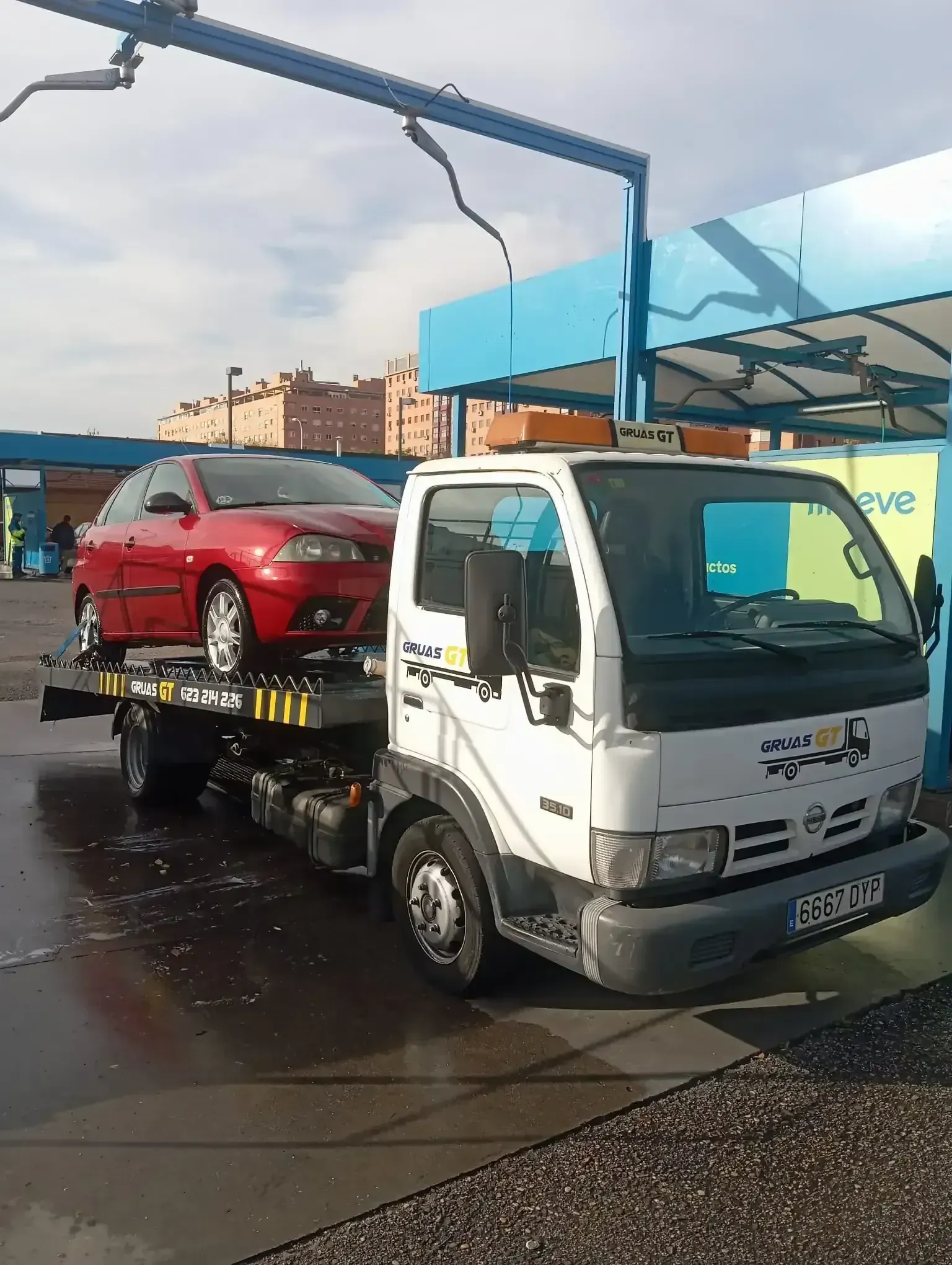 Grúa con un coche rojo en la plataforma, en un lavadero de coches.