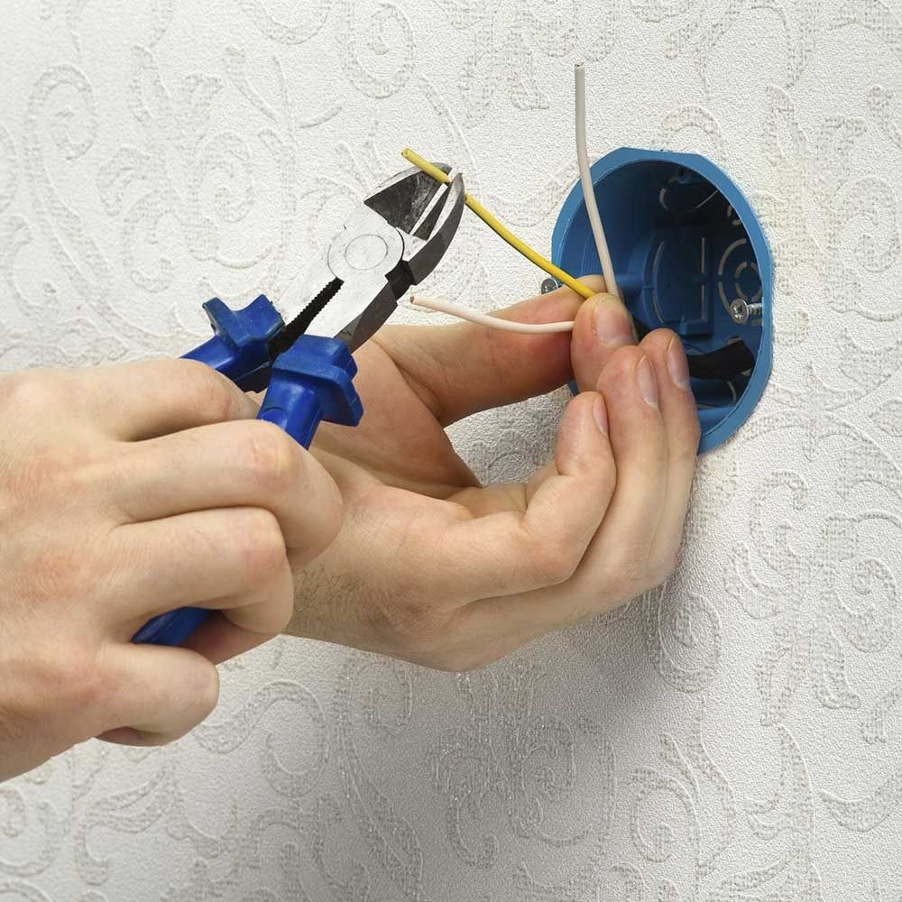 Persona que usa alicates para cortar un cable cerca de una caja eléctrica azul en una pared.