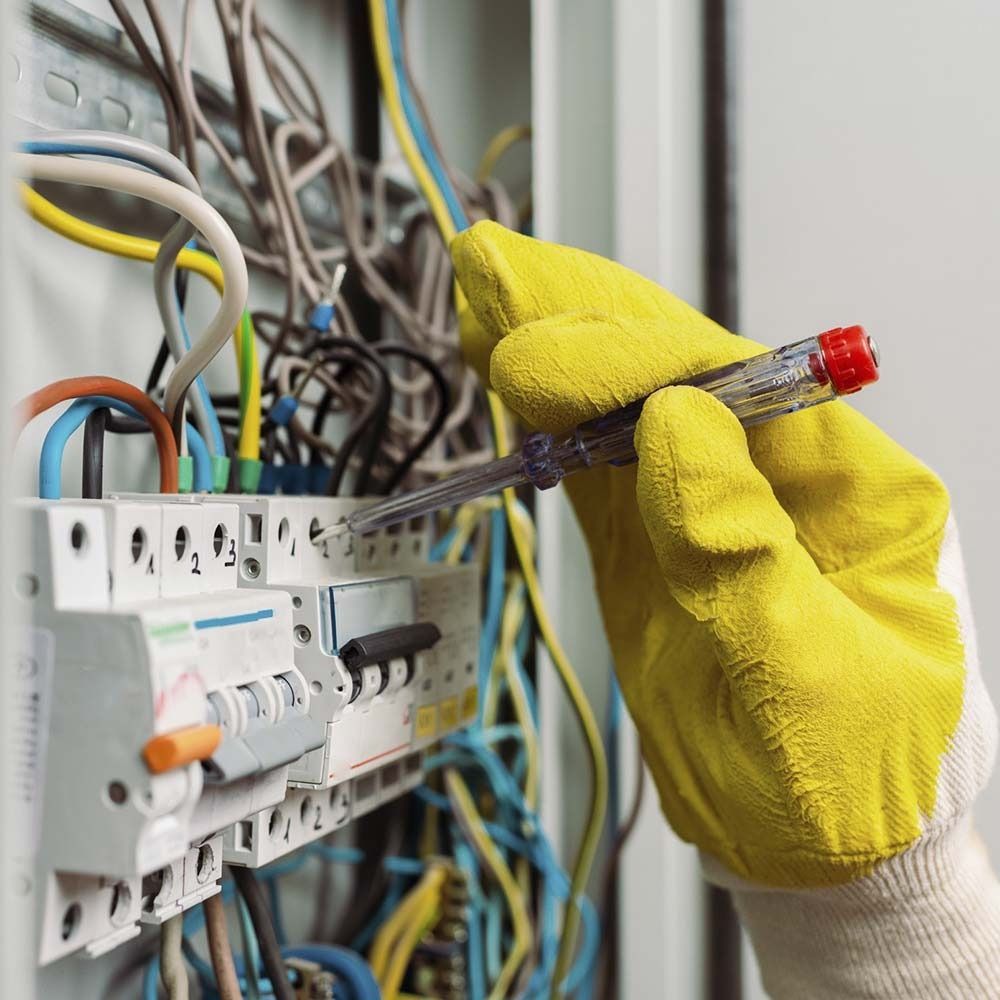Mano en guante amarillo probando el cableado eléctrico en un panel.