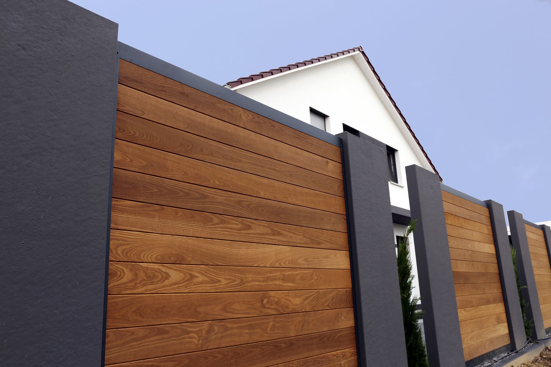Extérieur de maison moderne avec panneaux de clôture en bois, piliers gris foncé et toit à pignon blanc.