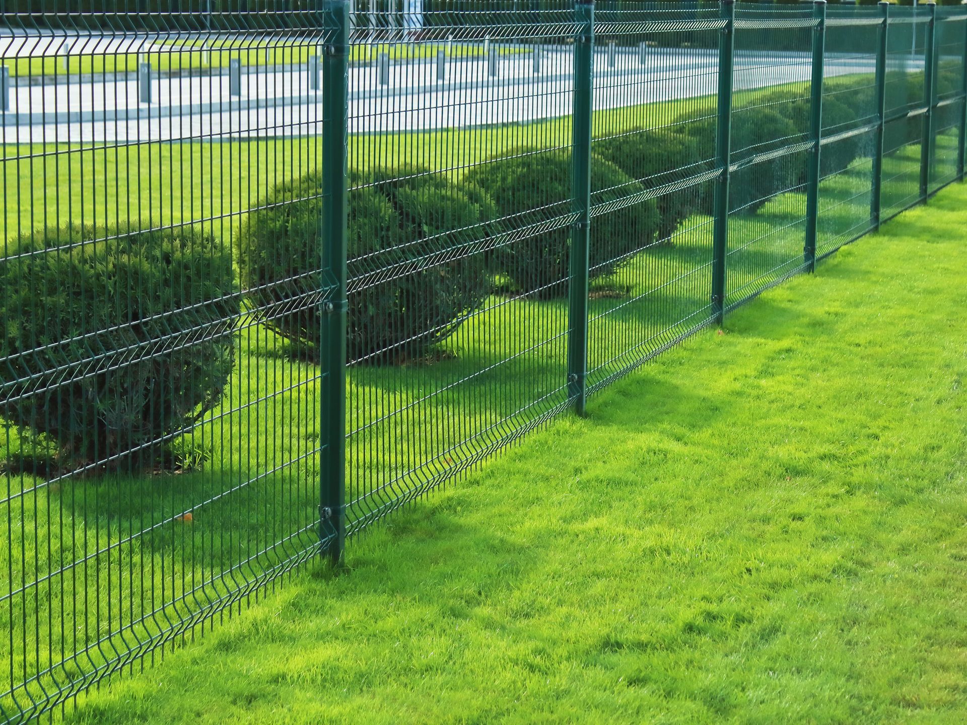 Clôture métallique verte bordant des haies soigneusement taillées et une pelouse verdoyante.