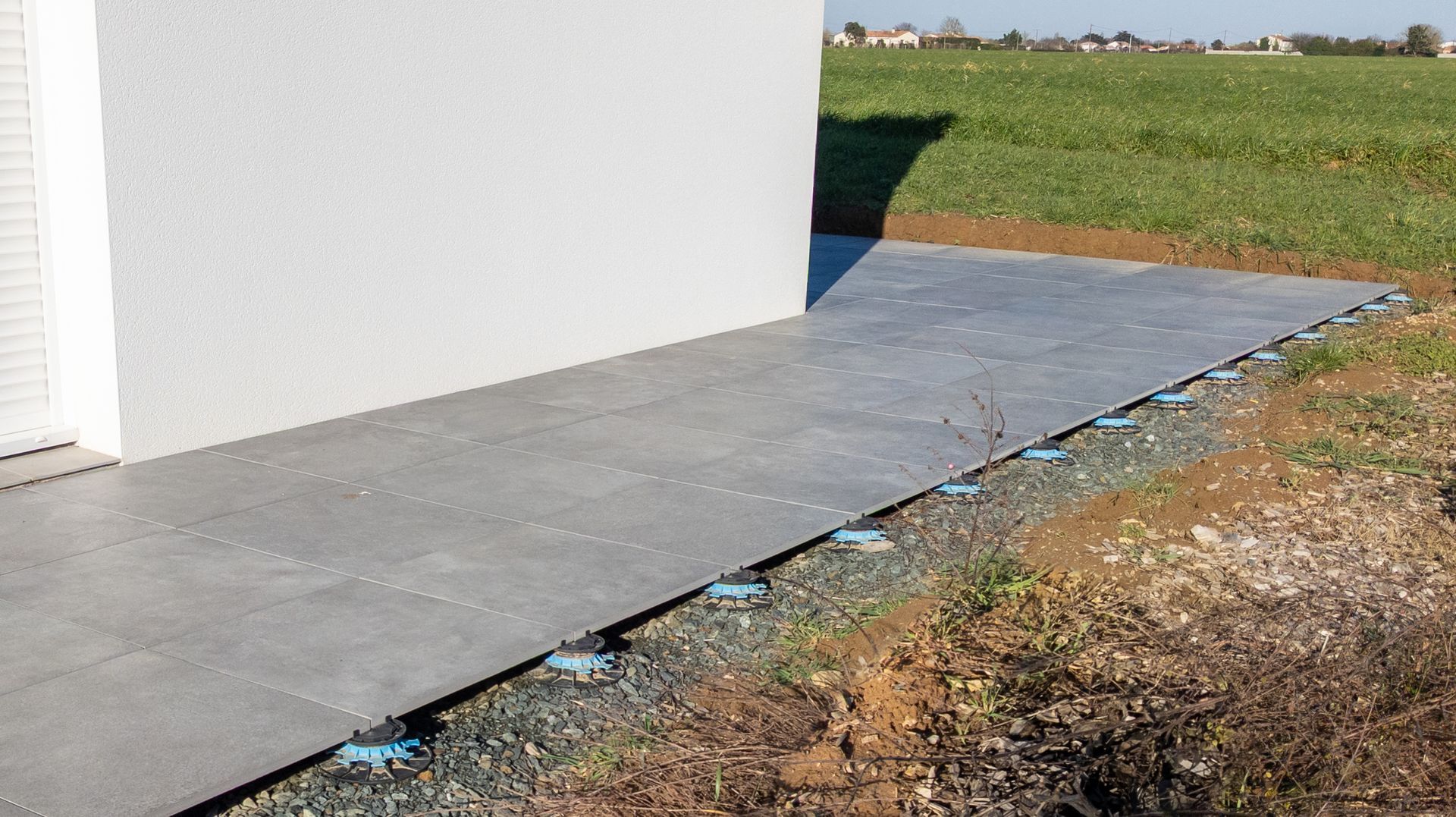 Allée en béton longeant un bâtiment blanc, avec une étroite bande bleue au sol.