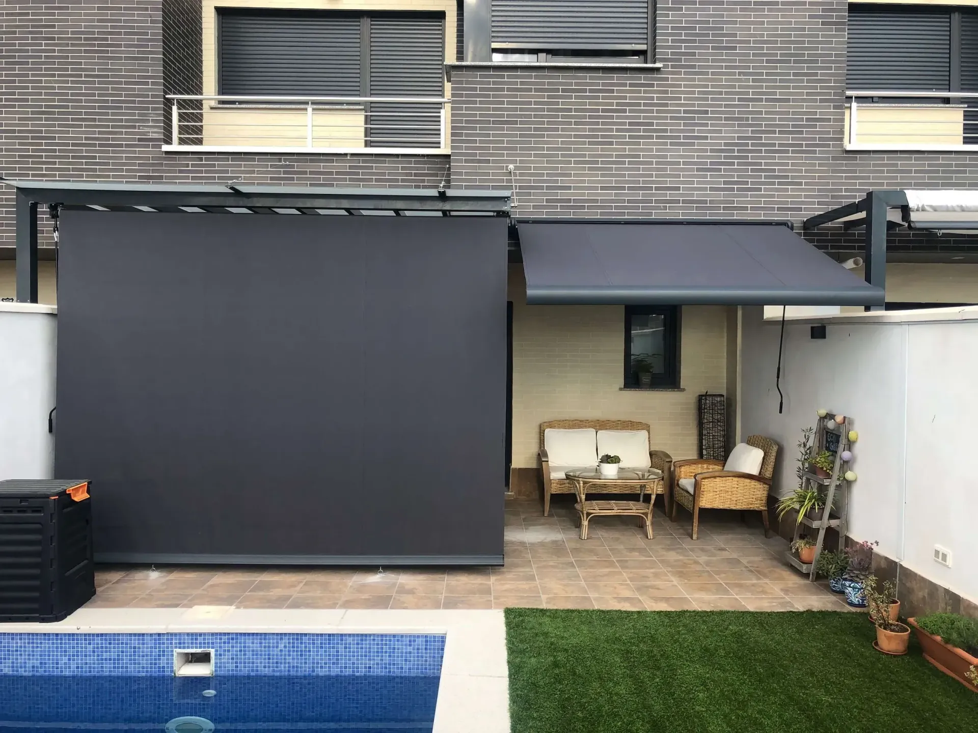 Patio trasero con una gran mampara retráctil oscura, zona de estar y piscina junto a una casa moderna.