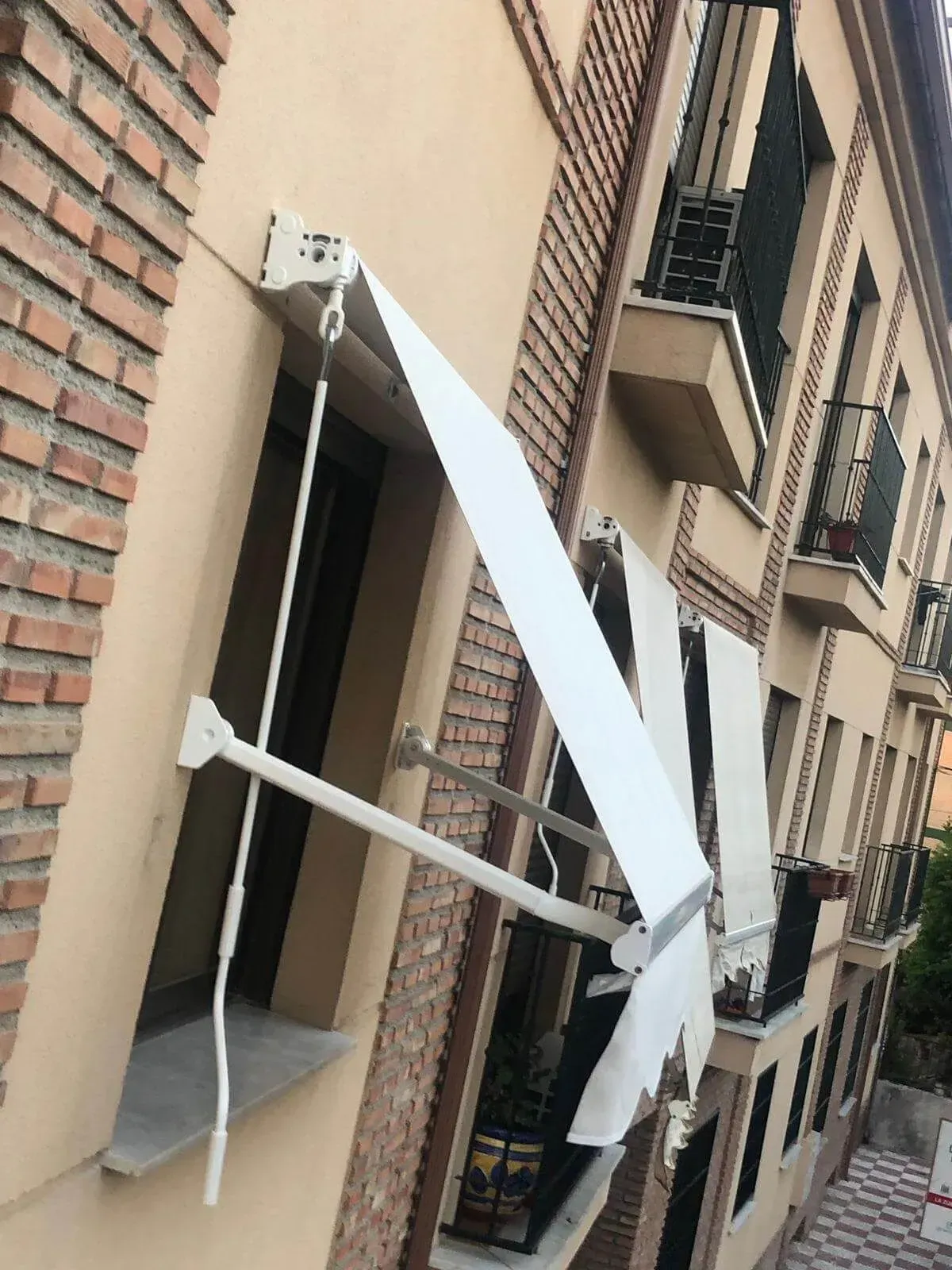 Toldo blanco dañado que cuelga sobre una ventana en la fachada de un edificio de apartamentos de ladrillo.