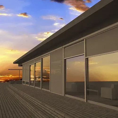 Casa moderna con grandes ventanales y terraza de madera al atardecer bajo un cielo colorido.