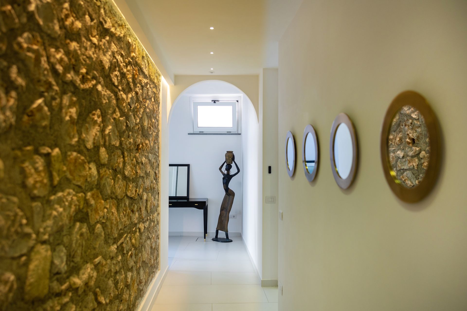 Hallway with stone wall, arched doorway, mirrors, and sculpture.