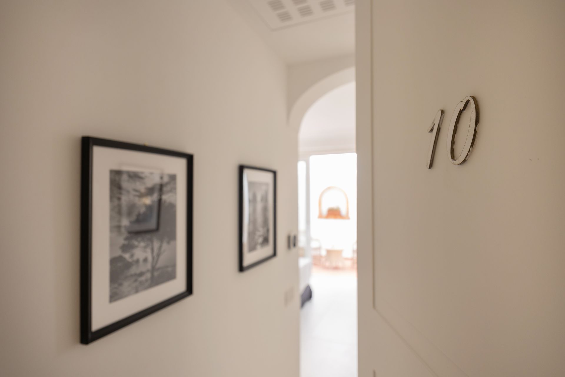 White hallway with framed art. Doorway with number 10, leading to a bright interior.