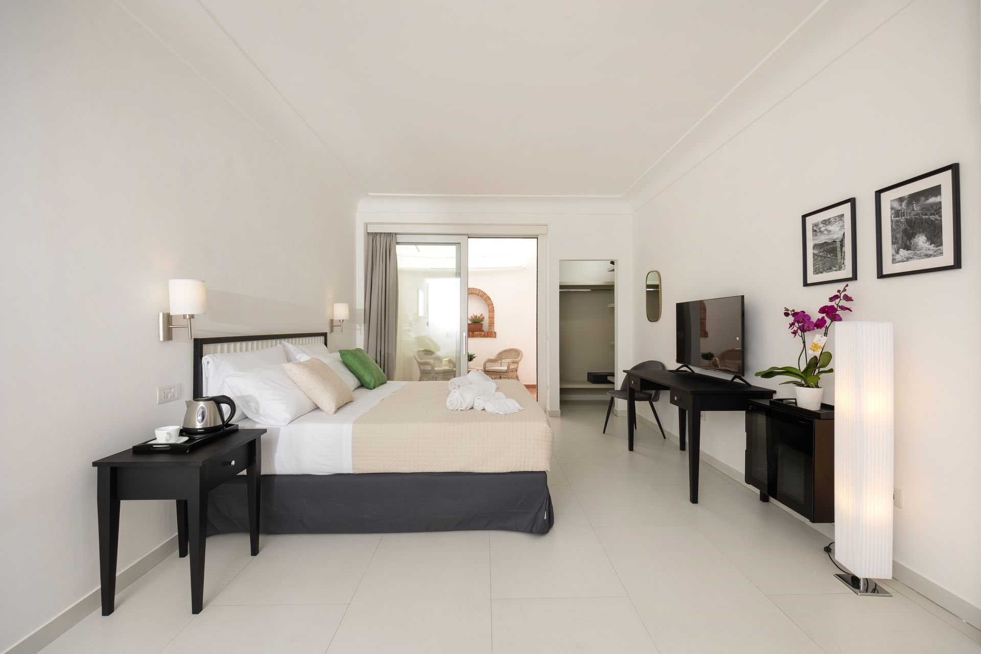 Hotel room with white walls, a bed, desk, TV, and balcony access.