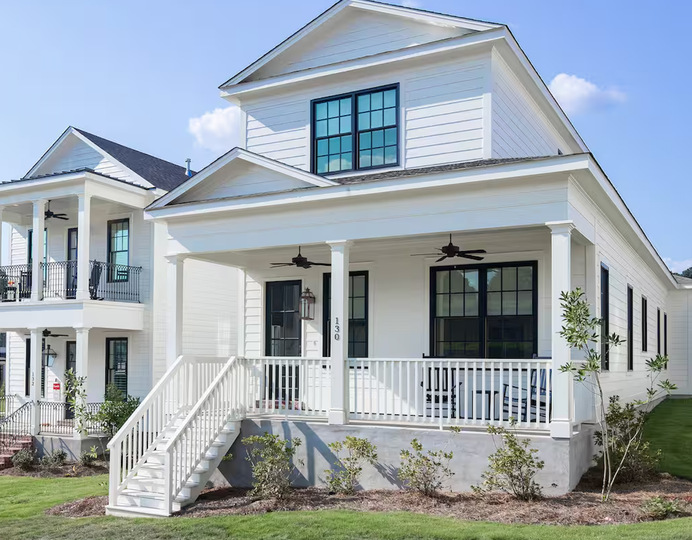 White two-story house with front porch, stairs, and black-trimmed windows under a blue sky