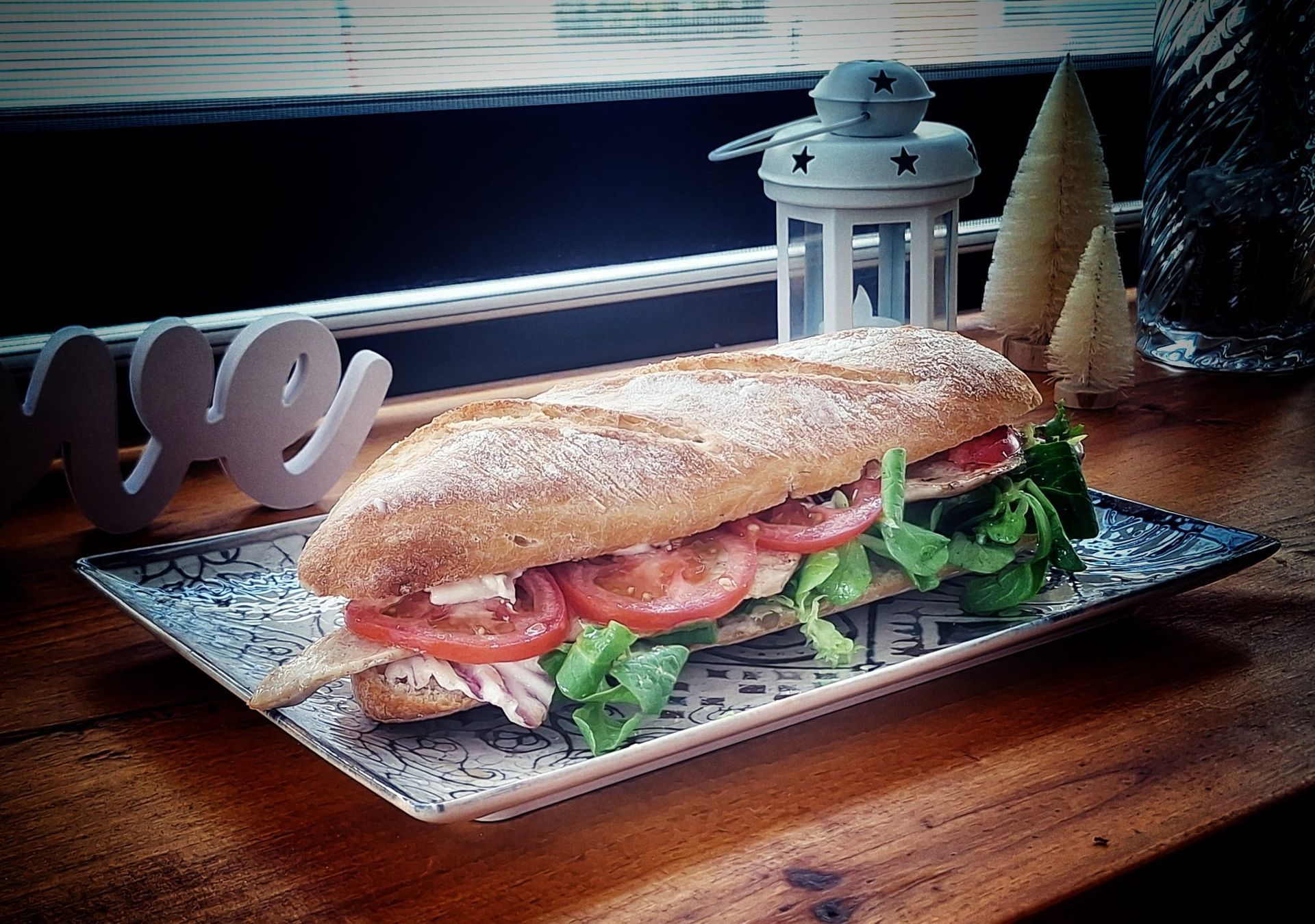 Un sándwich largo con atún, huevos y tomates sobre una mesa de madera.