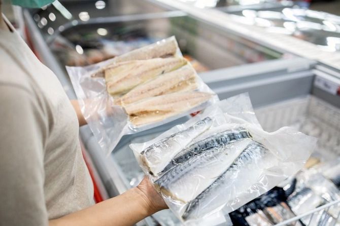 Una mujer sostiene una bolsa de pescado frente a un congelador.